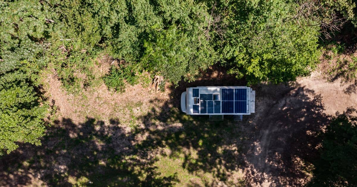 Letecký pohled na obytnou dodávku se solárními panely na střeše, zaparkovanou na lesní mýtině