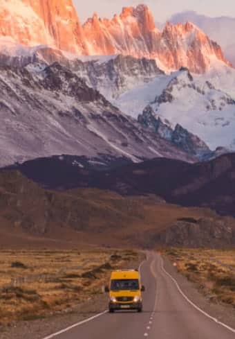 Žlutá obytná dodávka na otevřené silnici pod zasněženým masivem Fitz Roy v Patagonii